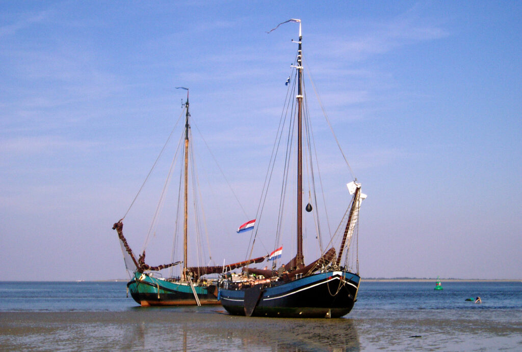 Twee platbodem schepen die drooggevallen zijn op een zandplaat op de waddenzee.